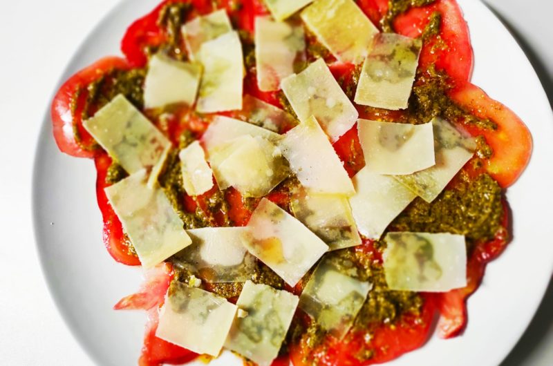 Carpaccio de tomate azul con salsa al pesto y láminas de queso parmesano.